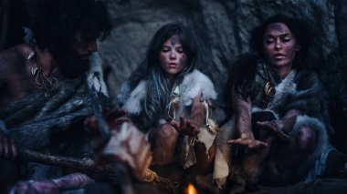 Tarih öncesi avcı-toplayıcı kabilesi Hayvan Derisi Giyen Gece Mağarada Yaşıyor. Neanderthal Ailesi Şenlik Ateşi 'nde Isınmaya Çalışıyor, Ateşin Üzerinde Elele tutuşuyor, Yemek Pişiriyor. Sıcak Filtre ile çekilmiş..