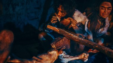 Neandertal 'in ya da Homo Sapiens Ailesi' nin Şenlik Ateşi Üzerine Hayvan Etleri Pişirip Yemesi 'nin yakın plan çekimi. Tarih öncesi avcı-toplayıcı kabilesi Gece vakti Karanlık Mağarada Hayvan Derileri Giyiyor