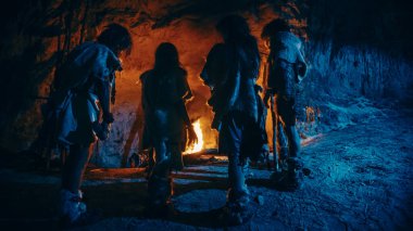Tarih öncesi avcı-toplayıcı kabilesi Hayvan Derisi Giyen Gece Bir Mağarada Yaşıyor. Neanderthal ya da Homo Sapiens Ailesi Şenlik Ateşi 'nde Isınmaya Çalışıyor, Ateşin Üzerinde Eller Tutuşuyor. Arka Görünüm