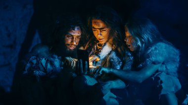 Tarih Öncesi, İlkel Avcı-Toplayıcılar kabilesi Hayvan Derisi Giyen Bir Mağarada Gece Akıllı Telefon Kullanıyor. Neandertal Homo Sapiens Ailesi Cep Telefonunda İnternet Taraması