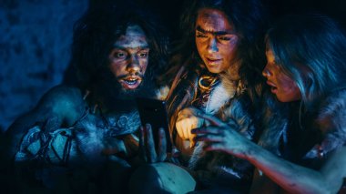 Tarih Öncesi, İlkel Avcı-Toplayıcılar kabilesi Hayvan Derisi Giyen Bir Mağarada Gece Akıllı Telefon Kullanıyor. Neandertal Homo Sapiens Ailesi Cep Telefonunda İnternet Taraması