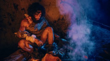 Mağarasında oturan hayvan derisi giyen ilkel mağara adamı portresi, ateşin yanında ısınıyor. İlkel mağara adamı Avcı Homo Sapiens Gece Kuyusunda Tek Başına