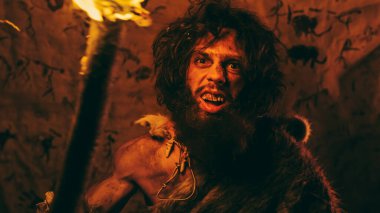 Hayvan derisi giyen ilkel mağara adamı portresi geceleri mağarasında duruyor, meşaleyi ateşle tutuyor ve saldırıyor. İlkel Neandertal Avcı Homo Sapiens Çığlık ve Tehdit