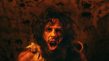 Hayvan derisi giyen ilkel mağara adamı portresi geceleri mağarasında duruyor, meşaleyi ateşle tutuyor ve saldırıyor. İlkel Neandertal Avcı Homo Sapiens Çığlık ve Tehdit