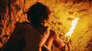 Primeval Caveman Wearing Animal Skin Standing in His Cave At Night, Holding Torch with Fire Looking at Drawings on the Walls at Night. Cave Art with Petroglyphs, Rock Paintings. Back View clipart