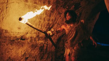 Primeval Caveman Wearing Animal Skin Exploring Cave At Night, Holding Torch with Fire Looking at Drawings on the Walls at Night. Neanderthal Searching Safe Place to Spend the Night clipart