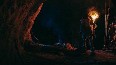 Hayvan derisi giyen ilkel mağara adamı geceleri bir mağarada durur, geceleri mağaradan dışarı bakan alevlerle meşaleyi tutar. Arka Görünüm