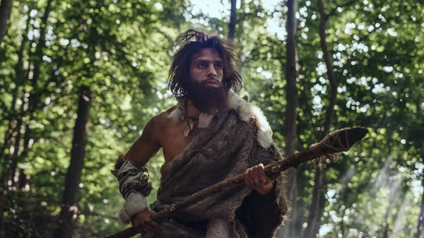 Portret van een oerholbewoner die dierenhuid en bontjacht draagt met een stenen speer in het prehistorische bos. Prehistorische Neanderthaler Hunter Scavenging met primitieve gereedschappen in de Jungle — Stockfoto