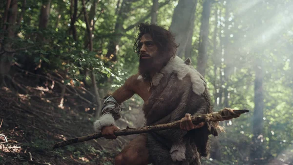 Retrato del cavernícola primitivo con piel de animal y piel de caza con una lanza de punta de piedra en el bosque prehistórico. Prehistórico Neanderthal Hunter listo para lanzar lanza en la selva — Foto de Stock