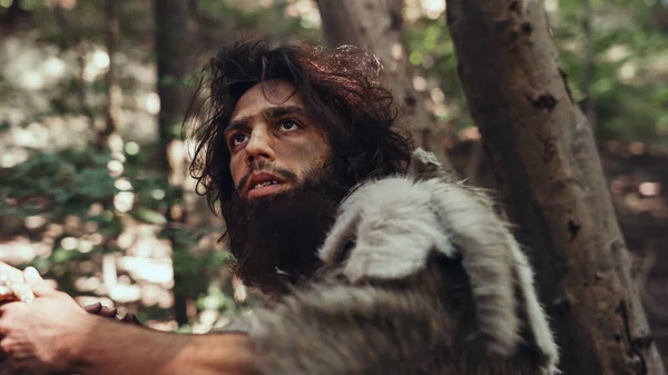 Nahaufnahme Porträt eines Höhlenmenschen, der Tierhaut und Pelz mit einem steinernen Speer im Urwald trägt. Urzeitlicher Neandertaler-Jäger bereit, Speer in den Dschungel zu werfen — Stockfoto