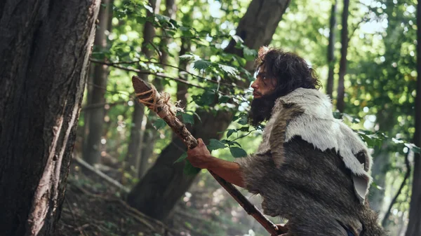 Porträt eines Höhlenmenschen mit Tierhaut und Pelz auf der Jagd mit einem steinernen Speer im Urwald. Urzeitlicher Neandertaler-Jäger bereit, Speer in den Dschungel zu werfen — Stockfoto