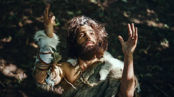 Portret pierwotnego jaskiniowca noszącego zwierzęcą skórę podnosi ręce do nieba Patrząc na słońce, mając pogańskie doświadczenie religijne. Prehistoryczny neandertalczyk wierzący i modlący się do Boga. Strzał pod wysokim kątem — Zdjęcie stockowe