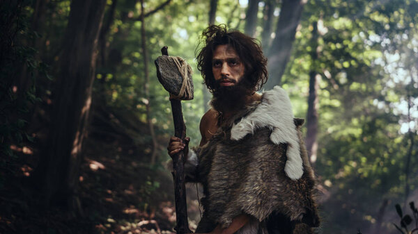 Portrait of Primeval Caveman Wearing Animal Skin and Fur Hunting with a Stone Tipped Hammer in the Prehistoric Forest. Prehistoric Neanderthal Ready to Attack Prey