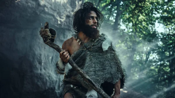 Pierwotny jaskiniowiec noszący zwierzęcą skórę trzyma kamienny młot Wychodzi z jaskini i rozgląda się po prehistorycznym krajobrazie, gotowy do polowania na zwierzęta. Neandertalczyk jedzie na polowanie w dżungli — Zdjęcie stockowe
