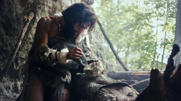 Pierwotny Jaskiniowiec noszący skórę zwierzęcą uderza w skałę ostrym kamieniem i sprawia, że pierwsze prymitywne narzędzie do polowania na ofiary zwierząt lub do obsługi skór. Neandertalczyk używający Handaxa. Świt cywilizacji ludzkiej — Zdjęcie stockowe