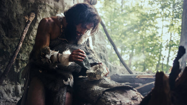 Primeval Caveman Wearing Animal Skin Hits Rock with Sharp Stone and Makes First Primitive Tool for Hunting Animal Prey or to Handle Hides. Neanderthal Using Handax. Dawn of Human Civilization