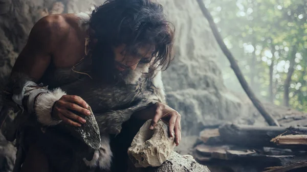 Zbliżenie Shot of Primeval Jaskiniowiec w Animal Skin Hits Rock z ostrym kamieniem, sprawia, że pierwsze prymitywne narzędzie do polowania na ofiary zwierząt. Neandertalczyk używający Flint Rock. Świt cywilizacji ludzkiej. — Zdjęcie stockowe