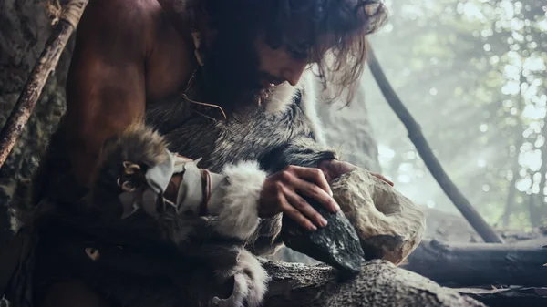 Hombre de las cavernas primitivo con piel de animal golpea roca con piedra afilada y hace herramienta primitiva para cazar presas de animales. Neanderthal usando hacha de mano para crear la primera rueda . — Foto de Stock