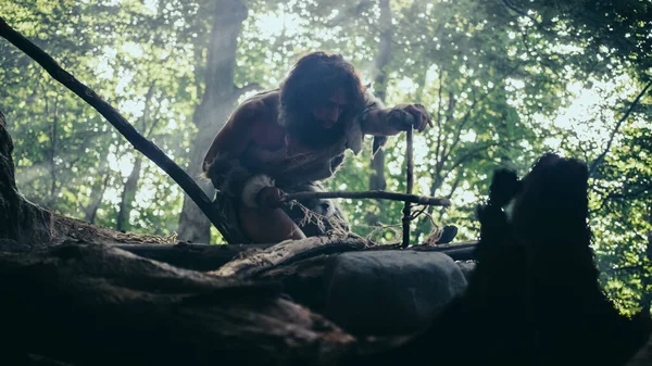 Silhuett av urtida grottman bär djur hud försöker göra en brand med båge borrmetod. Neandertalarnas Kindle Första konstgjorda eld i människans civilisationshistoria. Lågvinkelskott — Stockfoto