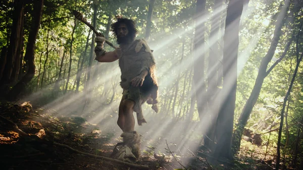 Retrato del cavernícola primitivo con piel de animal y piel de caza con una lanza de punta de piedra en el bosque prehistórico. Primitivo cazador neandertal listo para lanzar lanza en la selva — Foto de Stock