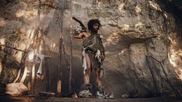 Primeval Caveman bär djur hud håller sten tippad hammare ser runt förhistorisk skog, redo att jaga djur byte. Neandertalarnas jakt i djungeln. — Stockfoto