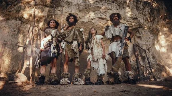 Tribo de quatro caçadores-coletores vestindo pele animal segurando ferramentas de ponta de pedra, dose na entrada de sua caverna. Retrato de dois adultos do sexo masculino e dois do sexo feminino Neandertais e seu modo de vida — Fotografia de Stock
