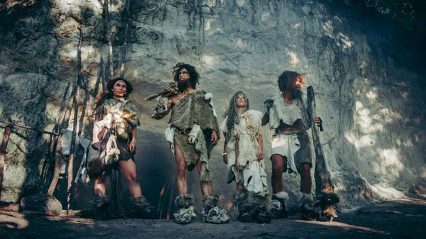 Tribe of Four Hunter-Gatherers in Animal Skin Holding Stone Tipped Tools, Pose at Entrance of Their Cave Портрет неандертальської сім'ї та їх спосіб життя. Постріл виконано з холодним фільтром — стокове фото