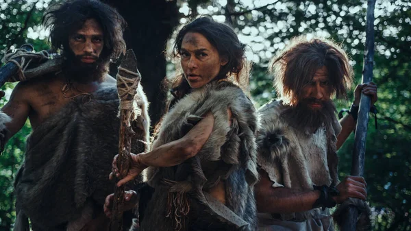 Kvinnlig ledare och två primitiva grottmän krigare hota fienden med sten tippade spjut, Skrik, försvara sin grotta och territorium i förhistoriska tider. Neandertalare Homo Sapiens stam — Stockfoto