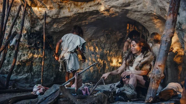 Tribù di cacciatori-raccoglitori che indossano pelle animale vivono in una grotta. Leader porta preda animale da caccia, cucina femminile cibo sul falò, ragazza disegno su Wals creazione di arte. Famiglia Neanderthal Homo Sapiens — Foto Stock