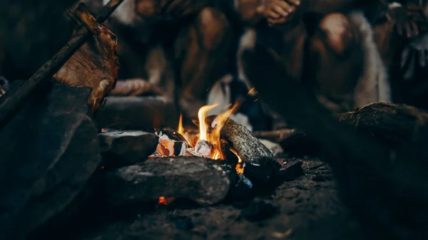 Detailní záběr prehistorických lovců-sběračů, kteří se snaží zahřát u ohně, držet ruce nad ohněm, vařit jídlo. Rodina neandrtálců nebo Homo Sapiens žijí v jeskyni v noci. — Stock fotografie