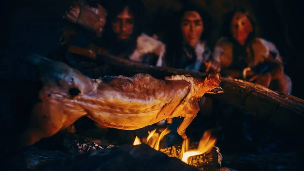 Крупный план "Homo Sapiens Family Cooking Animal Meat over Bonfire", а затем "Eating it". Племя доисторических охотников-собирателей в шкурах животных, питающихся ночью в темной страшной пещере . — стоковое фото