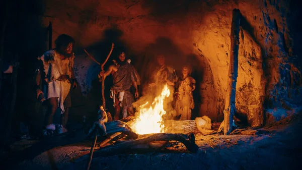 Kmen pravěkých lovců a sběračů, kteří nosí zvířecí kůže, stojí v noci kolem ohně před jeskyní. Portrét neandrtálské rodiny Homo Sapiens při pohanském náboženském rituálu poblíž ohně — Stock fotografie