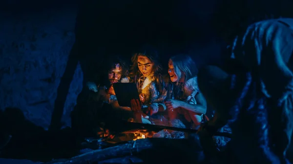 Tribe of Prehistoric, Primitive Hunter-Gatherers Wearing Animal Skins Use Digital Tablet Computer in a Cave at Night. Neanderthal or Homo Sapiens Family Browsing Internet, Watching Videos, Streaming — Stock Photo, Image