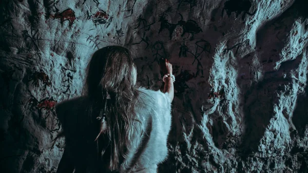 Powrót Widok prymitywnego prehistorycznego neandertalskiego dziecka w skórze zwierzęcia rysuje zwierzęta i streszczenia na ścianach. Tworzenie pierwszej sztuki jaskini z Petroglifów, Obrazy skalne. Strzał wykonany w nocy zimnym światłem — Zdjęcie stockowe