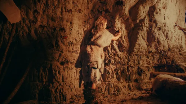 Обратный вид примитивного доисторического неандертальца, носящего шкуру животного, рисует животных и абстракты на стенах ночью. Создание первого пещерного искусства с петроглифами, наскальными рисунками . — стоковое фото
