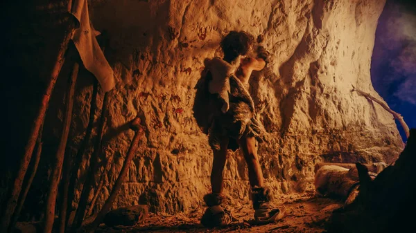 Обратный вид примитивного доисторического неандертальца, носящего шкуру животного, рисует животных и абстракты на стенах ночью. Создание первого пещерного искусства с петроглифами, наскальные рисунки, освещенные огнем — стоковое фото