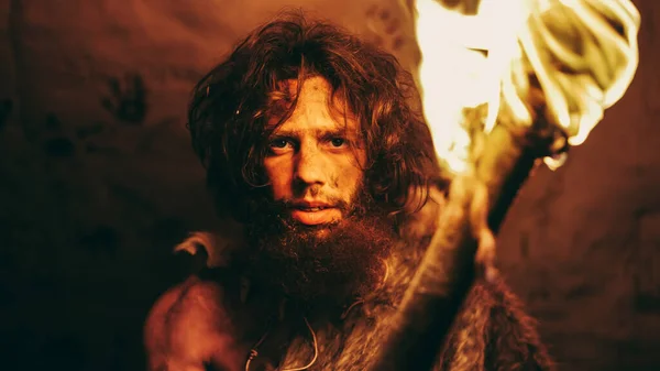 Портрет первозданної печери Caveman, що носить шкіру тварин, стоїть у своїй печері вночі, тримає факел з вогнем. Примітивний мисливець за неандертальцями Гомо Сапієнс вночі сам у своєму дні — стокове фото