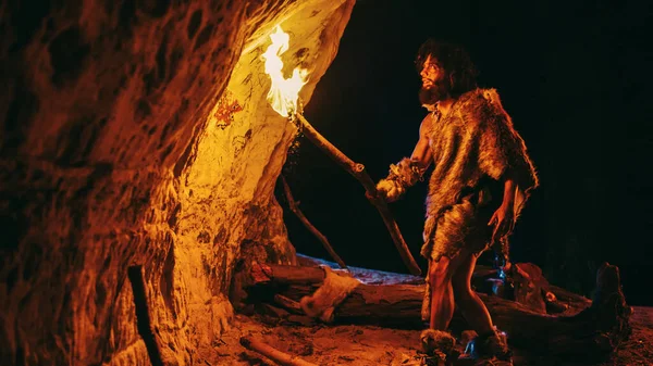 Первобытный пещерный человек в шкуре животного исследует пещеру ночью, держа факел с огнем, глядя на рисунки на стенах ночью. Пещерное искусство с петроглифами, наскальные рисунки. Вид сбоку — стоковое фото