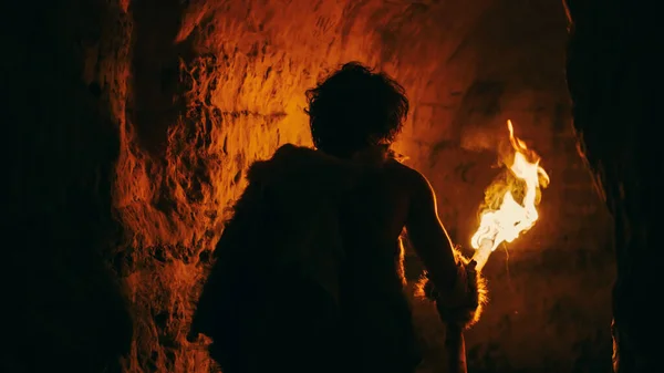 Primeval Caveman draagt Animal Skin Exploring Cave 's nachts Holding Torch met vuur Kijkend naar tekeningen op de muren' s nachts. Neanderthaler zoekt veilige plek om de nacht door te brengen. Achteraanzicht — Stockfoto