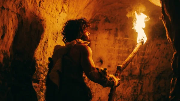 Portrait of Primeval Caveman Wearing Animal Skin Exploring Cave At Night, Holding Torch with Fire Looking at Drawings on the Walls at Night. Neanderthal Searching Safe Place to Spend the Night — Stock Photo, Image