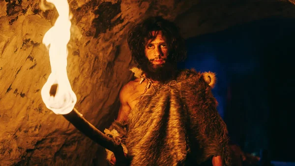 Πορτρέτο του αρχέγονου Caveman φορώντας το δέρμα των ζώων Exploring Cave τη νύχτα, κρατώντας πυρσό με φωτιά κοιτάζοντας σε κάμερα τη νύχτα. — Φωτογραφία Αρχείου