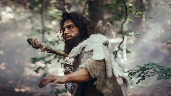 Первобытный пещерный человек, носящий шкуру животного, держит в руках каменное копье, исследует доисторический лес в поисках добычи животных. Някрошюс охотится в лесу — стоковое фото