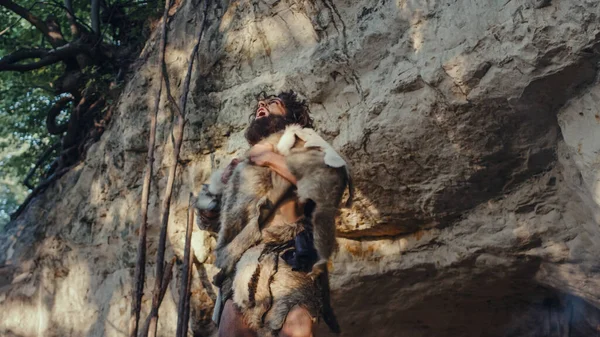 Portret pierwotnego jaskiniowca noszącego skórę zwierzęcą Bije i krzyczy klatka piersiowa, broniąc swojej jaskini i terytorium w prehistorycznym lesie. Prehistoryczny neandertalczyk lub przywódca Homo Sapiens — Zdjęcie stockowe