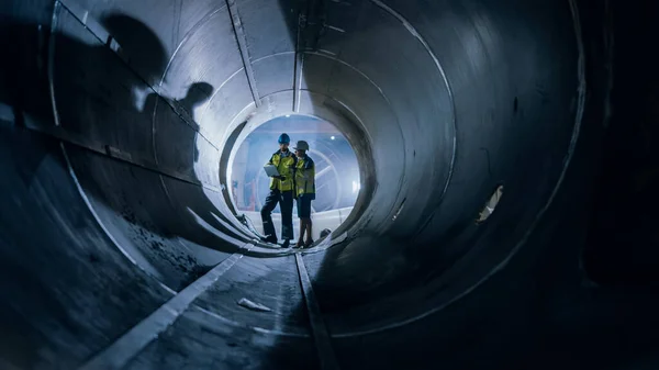 Två tunga industriingenjörer promenader Inside Pipe, Använd laptop, Har diskussion, Kontroll Design. Anläggning av rörledningen för olja, naturgas och bränslen. Fabriken för industriell tillverkning — Stockfoto