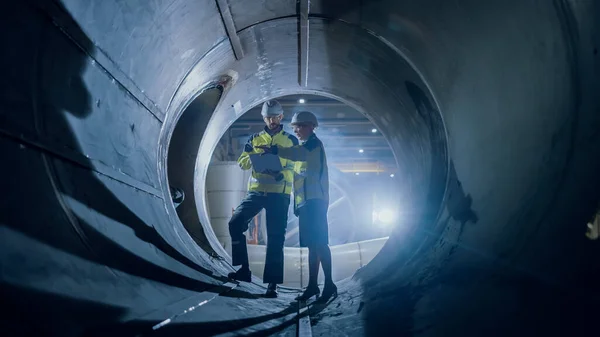 Dos ingenieros de la industria pesada que caminan dentro del tubo, utilizan el ordenador portátil, tienen discusión, comprobando diseño. Construcción del Gasoducto de Transporte de Petróleo, Gas Natural y Biocombustibles. Fábrica de fabricación industrial — Foto de Stock