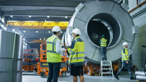 Dois engenheiros da indústria pesada caminham através da fábrica de fabricação de tubos, usam o computador tablet digital, discutem. Instalação para Construção de Produtos de Transporte de Petróleo, Gás e Combustível — Fotografia de Stock