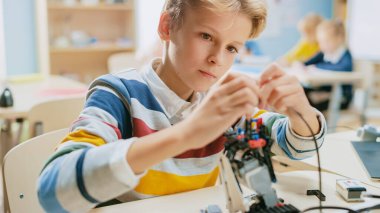 Smart Schoolboy Builds Constructs Small Robot and Uses Laptop to Program Software for Robotics Engineering Class. School Science Classroom with Gifted Brilliant Children Working with Technology clipart