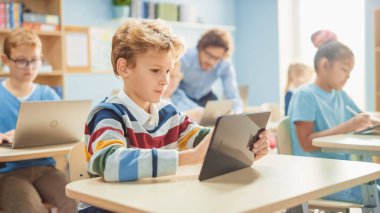 İlköğretim Okulu Bilgisayar Bilimi Sınıfı: Akıllı Çocuk Dijital Tablet Bilgisayar kullanıyor, onun sınıf arkadaşları da dizüstü bilgisayarlarla çalışıyor. Çocuklar BTMM 'de Modern Eğitim Alırken, Oynarken ve Öğrenirken