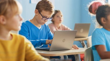 İlköğretim Okulu Bilgisayar Bilimi Sınıfı: Akıllı Çocuk Laptop kullanıyor, Sınıf arkadaşları laptoplarla çalışıyor, Herkes Öğretmeni Dikkatle Dinliyor. Çocuklar Modern Eğitime Gidiyor