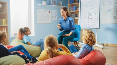 İlköğretim Okulu Yaratıcılık Sınıfı: Nazik Öğretmen Dijital Tablet Bilgisayarı kullanırken Çocuklar Torbaların Üzerinde Oturuyor. Akıllı Çocuklar Arkadaş Canlısı Modern Çevrede Öğreniyor